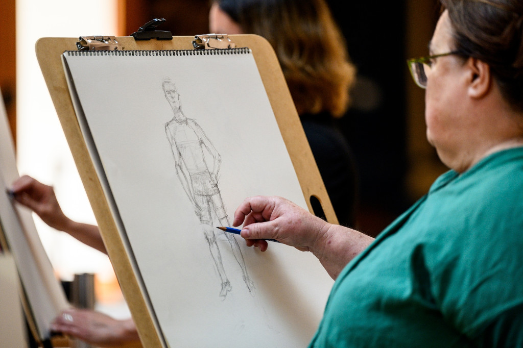 A hand chalks a drawing on a paper that's on an easel.