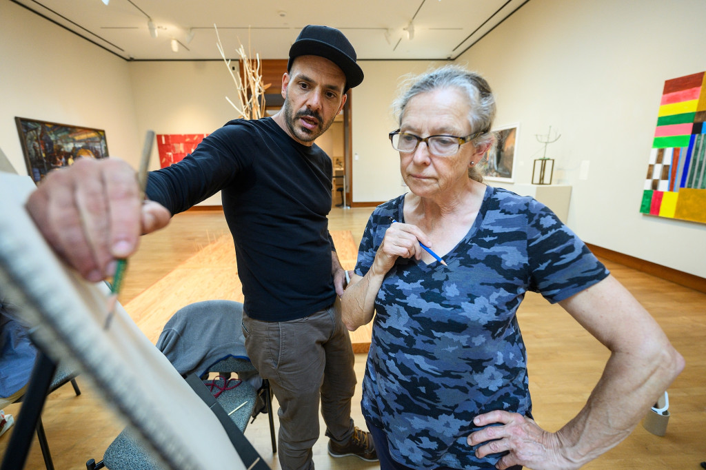 A man and a woman look at a drawing on an easel and talk.