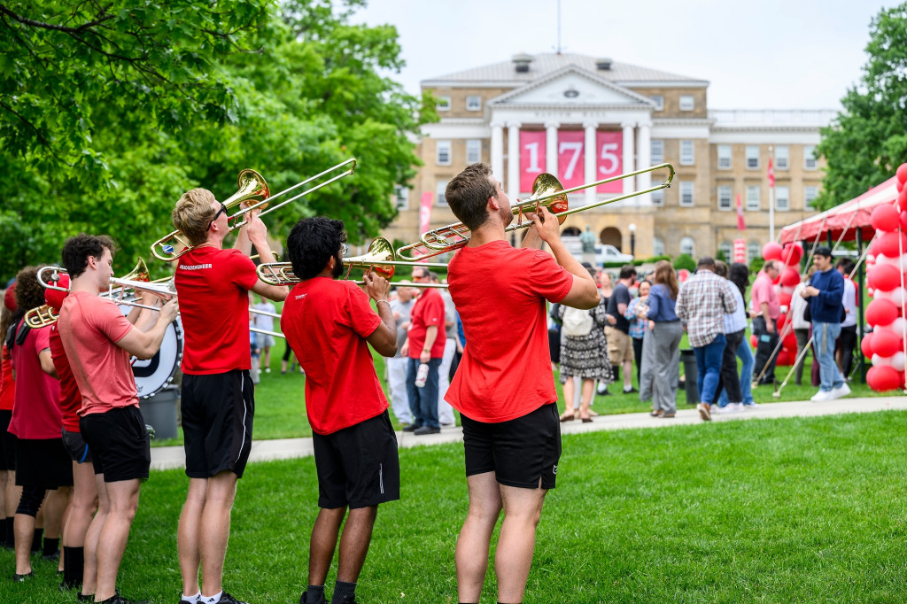 Band members wearing red play instruments while standing on a green lawn.