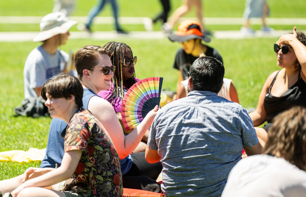 People sit on a sunny lawn, eat and talk. It's a picnic.