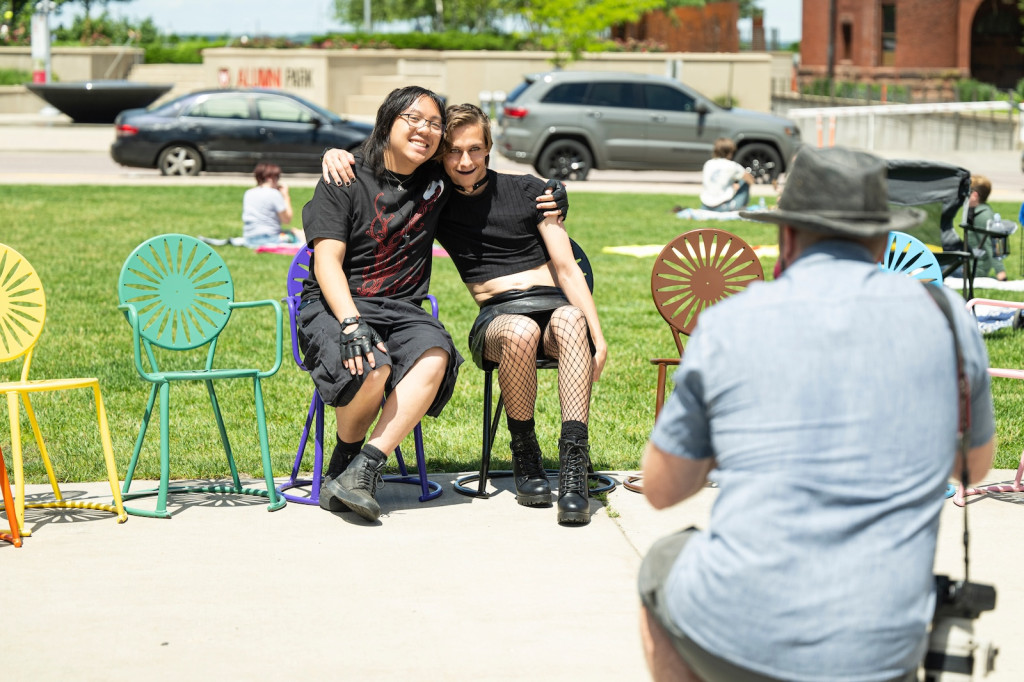 Two people sit on colorful chairs, and hug each other arm in arm.