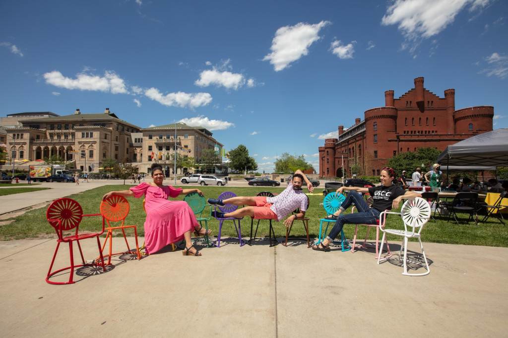 Three people lounge on rainbow colored chairs.