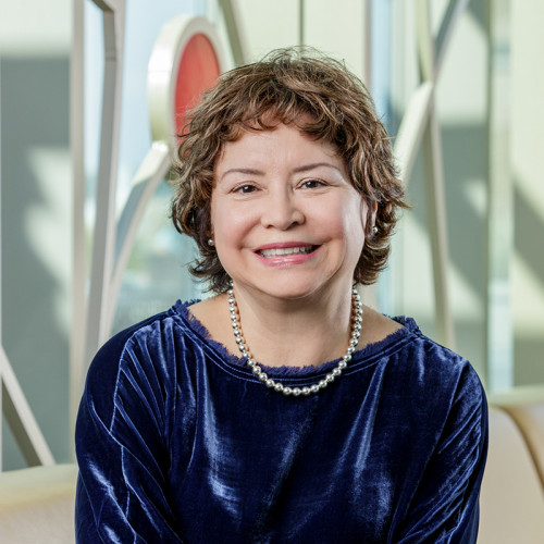 A Native American Indian woman, with light brown curly hair, wearing a royal blue dress with silver beads.