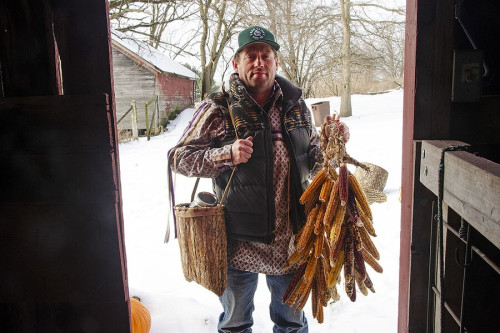 A man stands in a doorway holding corn and other food.