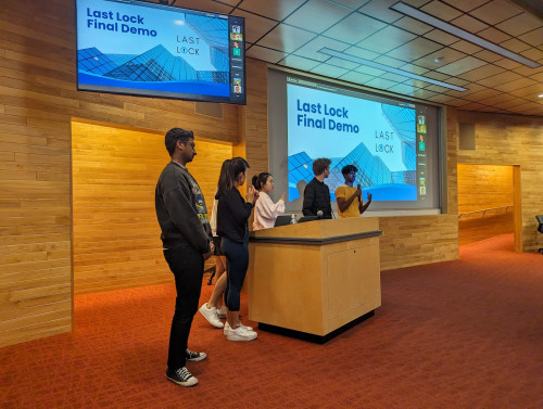 A group of people huddle around a podium, with several electronic displays on the wall behind them.