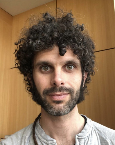 A person looking directly at the camera, in front of a wooden panel background