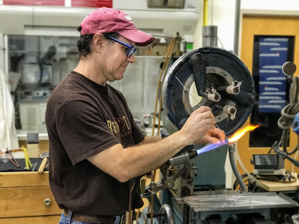 A man works at heavy machinery, creating a work of glass.