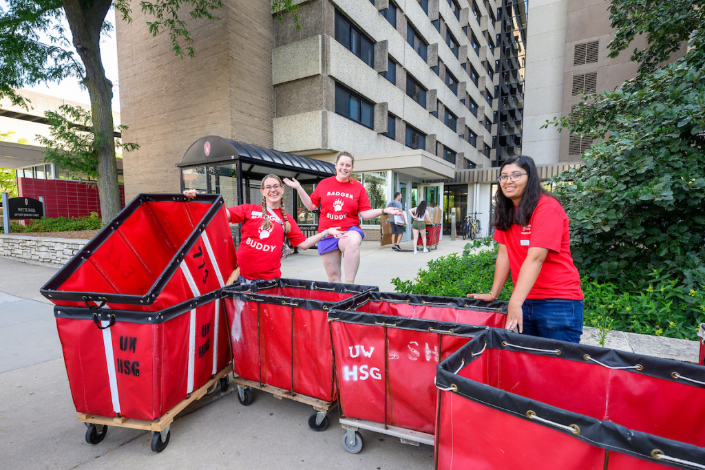 A group of people stand outside a building along with a number of red carts used for moving belongings into the residence halls.