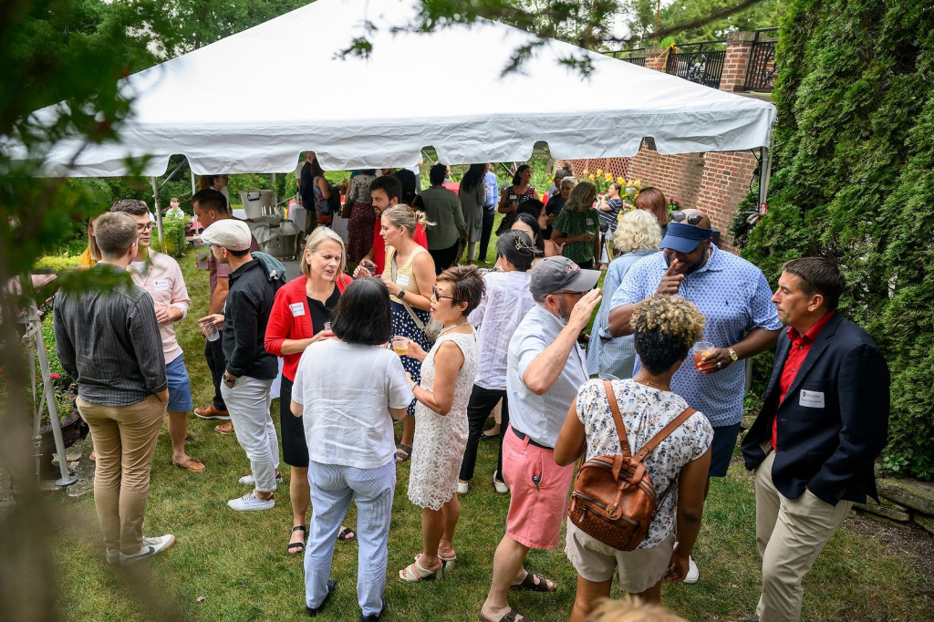 People mill around and talk on a grassy yard.