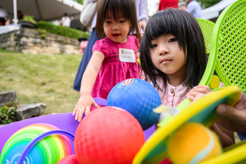 Two young kids play with toys on a lawn.