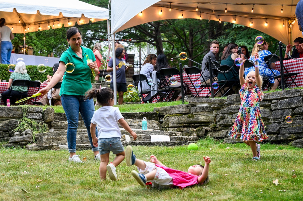 Three kids chase after bubbles that a woman is making with a bubble wand.