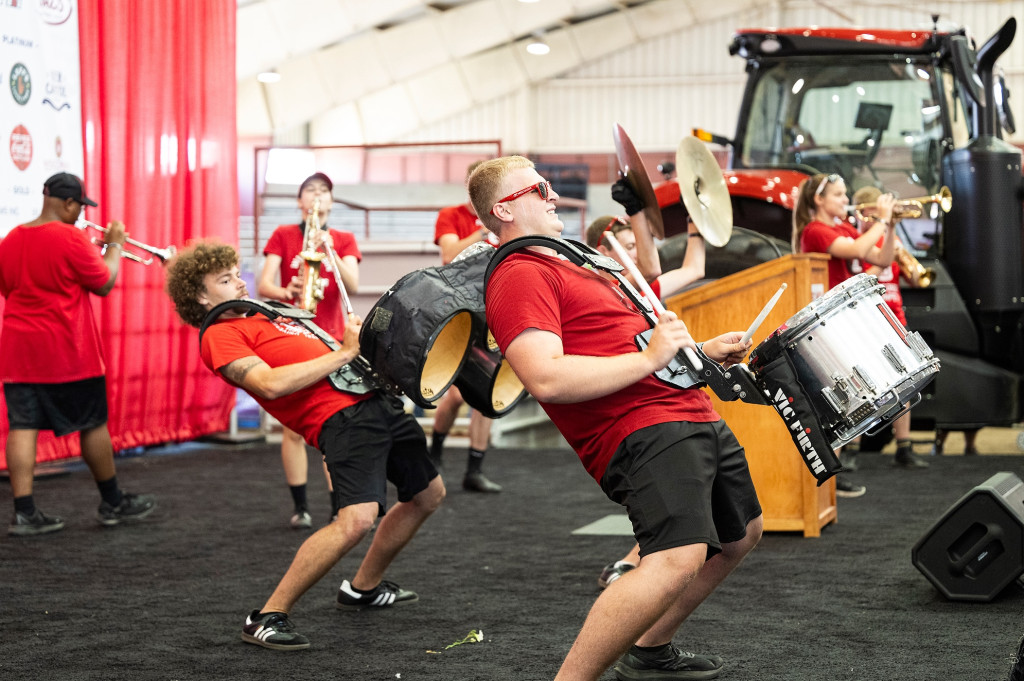 A group of drummers lean back while drumming during a band performance. 