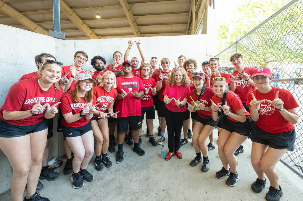 A group of people all in red shirts stand together and form their hands in to the shape of the letter W. 