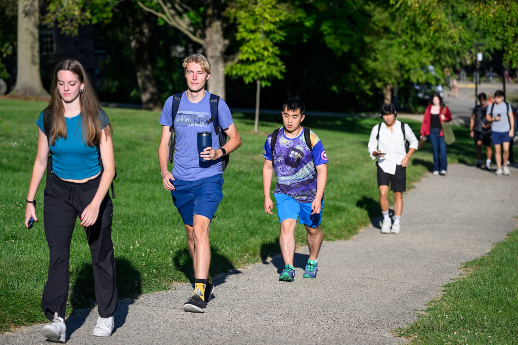 Several students wearing backpacks walk up a hill.