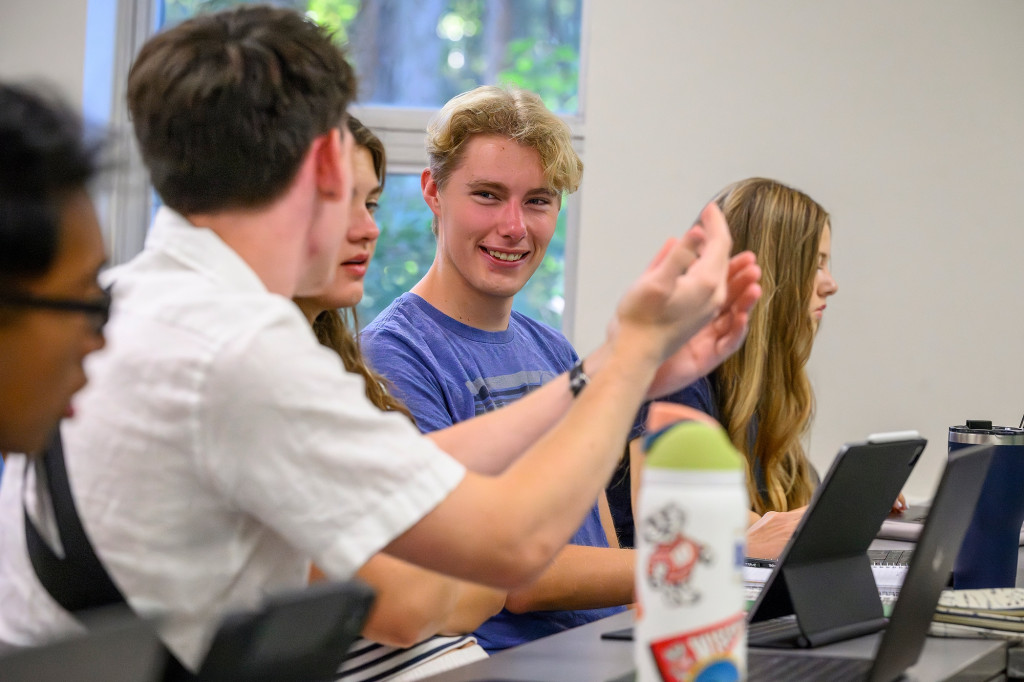 A student smiles in class, as he talks to classmates.