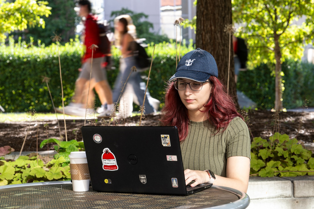 A woman sits at an outdoor table and works on her laptop.