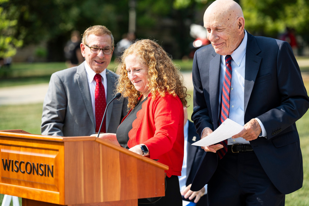 A woman and two men stand at a podium and smile and chat.