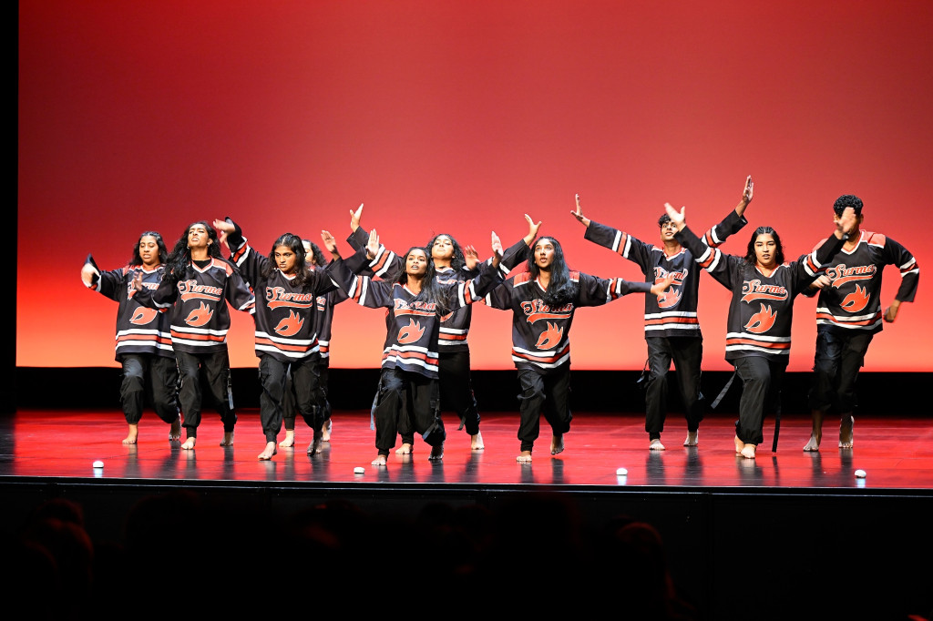 A number of people dance in a line on stage.