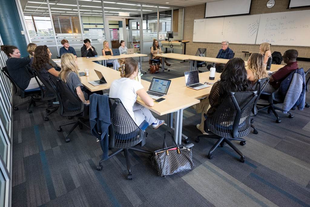 A series of tables in a rectangle formation is shown; seated at it are about a dozen people.