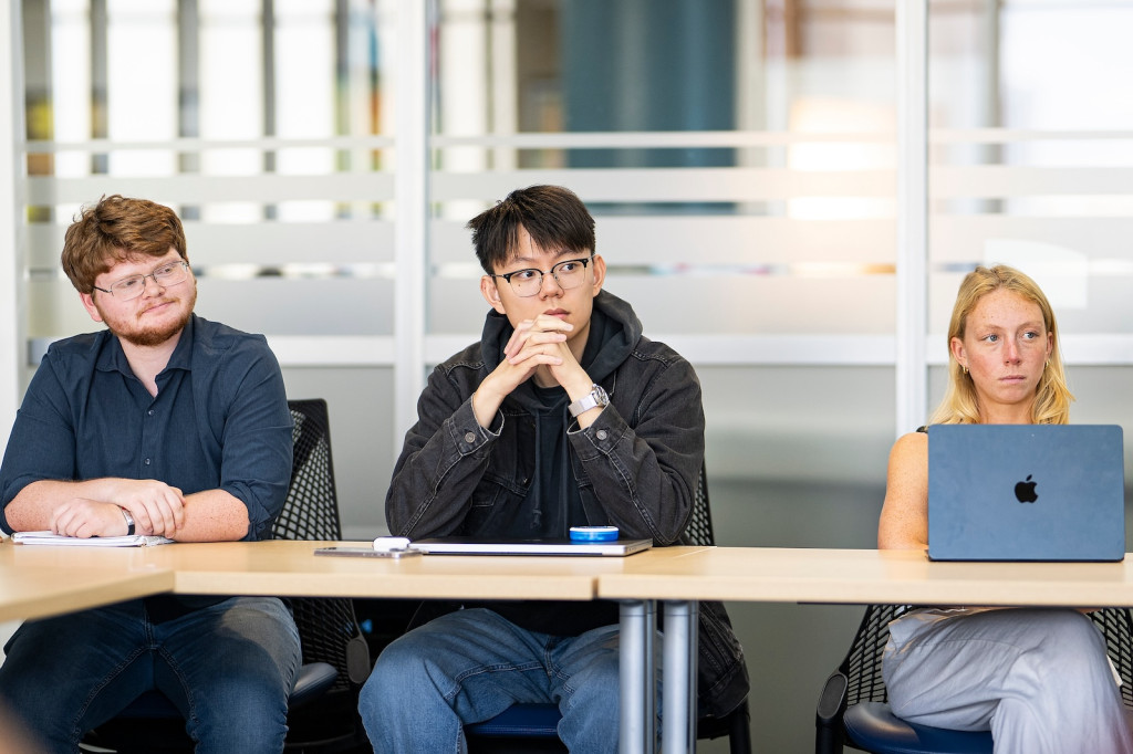 Three students sit at a table and attentively listen.