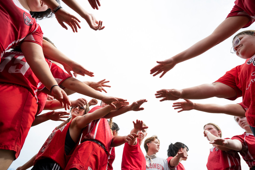 Women in red uniforms all bring their hands together in a photo taken from below.