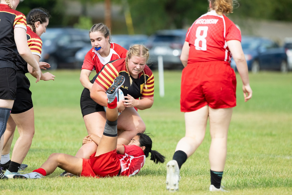 Two women in red team up to tackle an opponent in a black uniform.