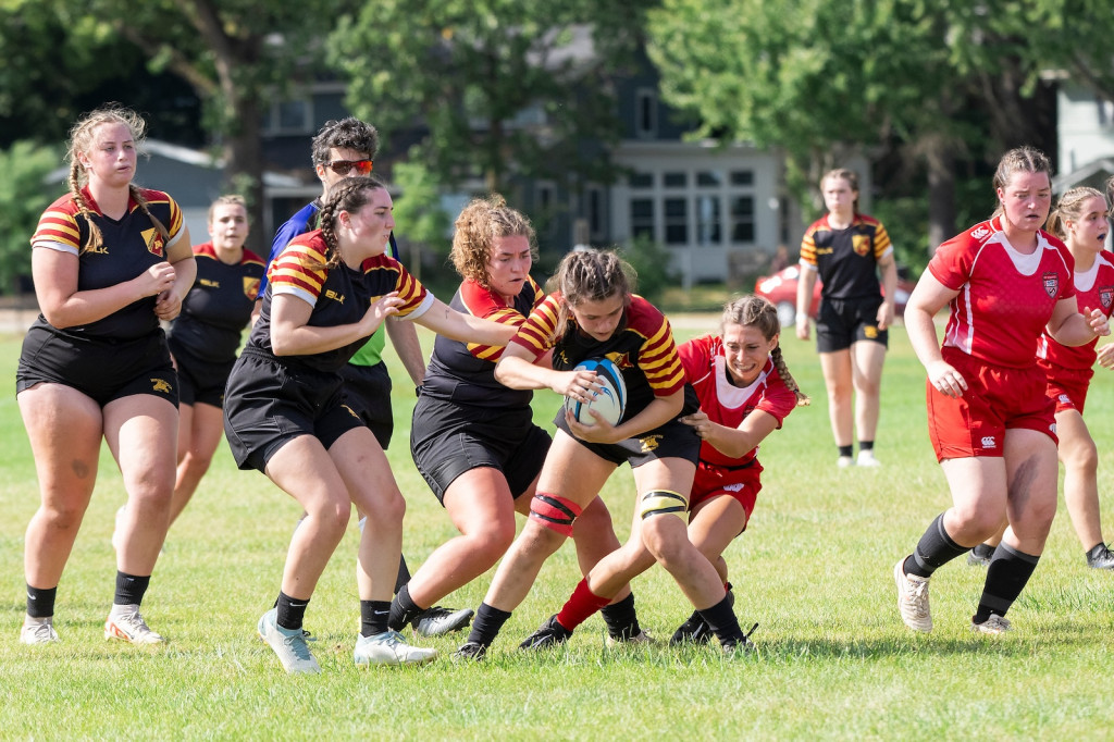 A woman tackles another woman holding a rugby ball.