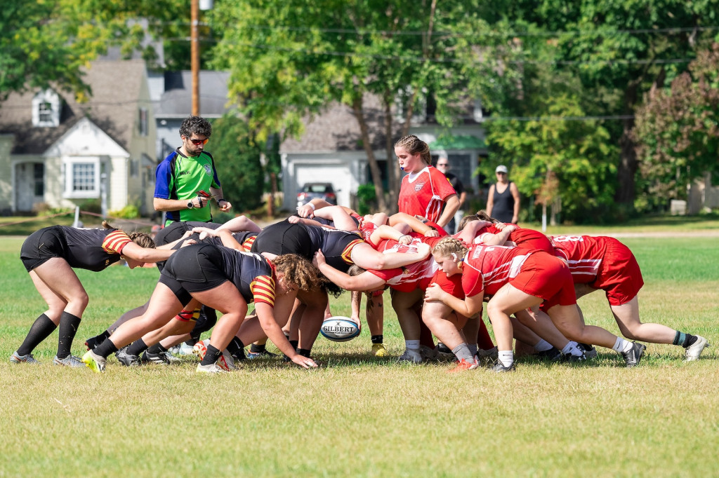 Two teams of women form a scrum, that is, players on each side crouch close to the ground in a group and push hard against the opposing team, also crouched to the ground.