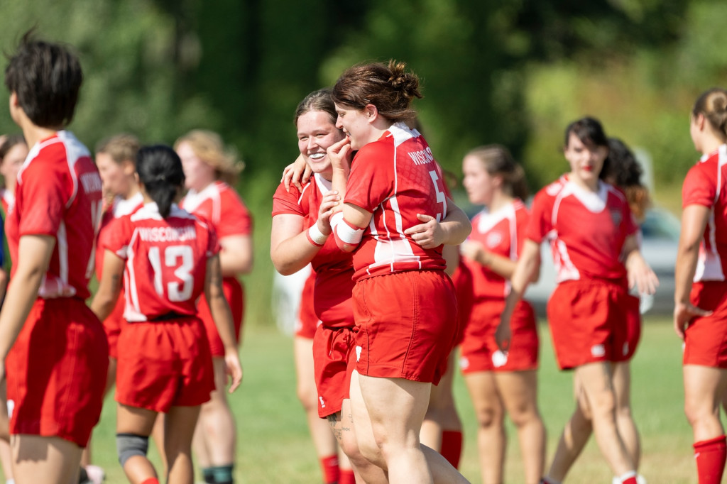 Two women in red uniforms smile and hug, as other players crowd in the background.