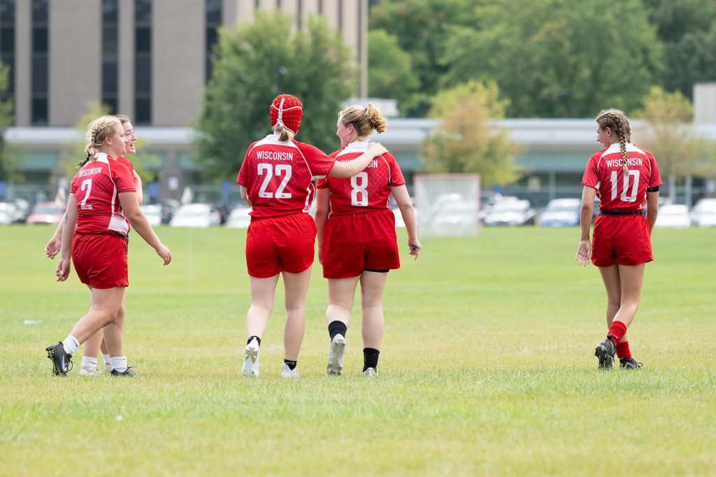 A woman in a red uniform walks off a field with another, her arm draped over her shoulder.