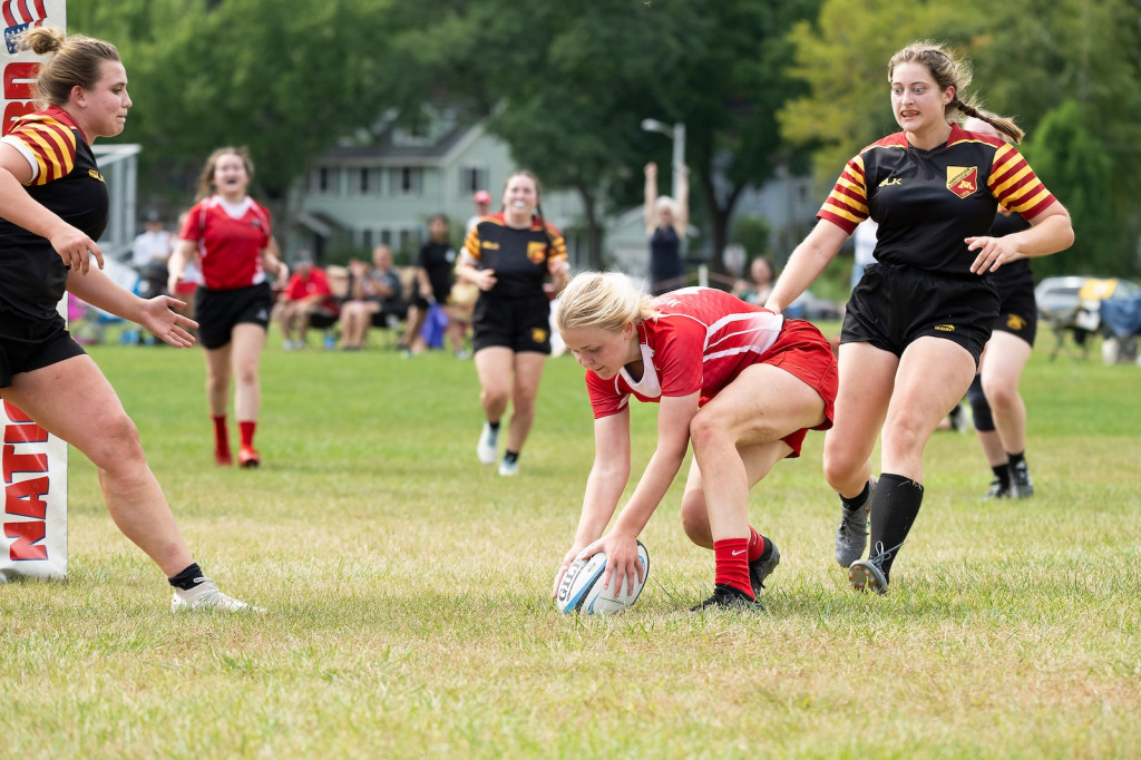 A woman sets a rugby ball down on the grass as others watch.