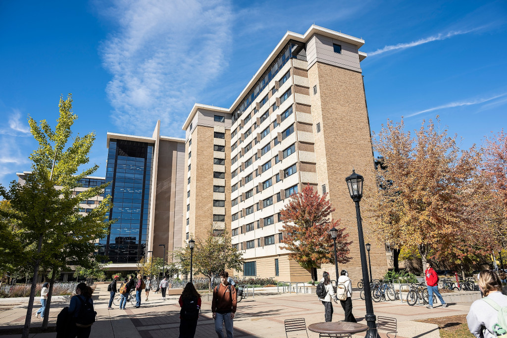 A high-rise building is shown in the sunlight while people walk in the foreground.