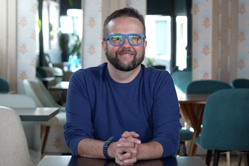 A bearded man wearing glasses smiles at the camera.