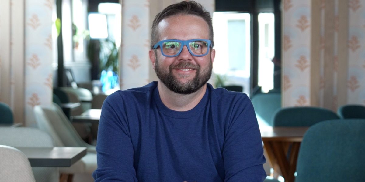 A bearded man wearing glasses smiles at the camera.