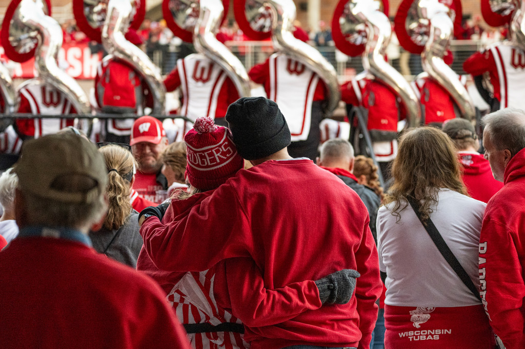 A group of people clad in red listen to a marching band.