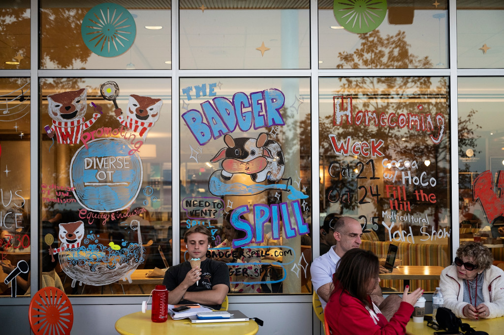 A person eats an ice cream cone. Windows behind him have several homecoming message and drawings painted on them.