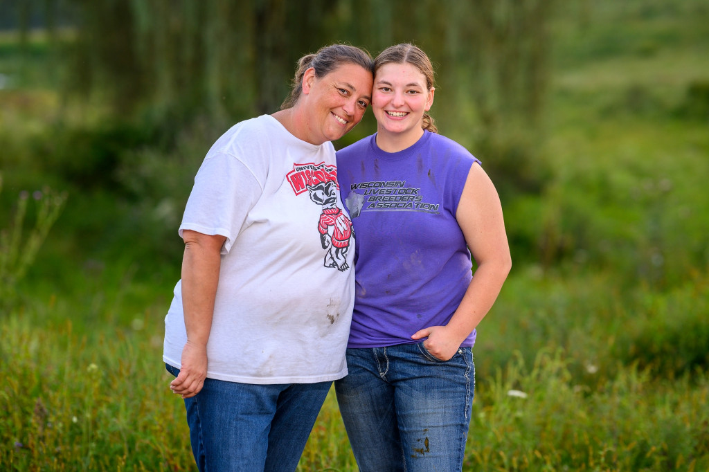 Two women smile for the camera and stand arm in arm.