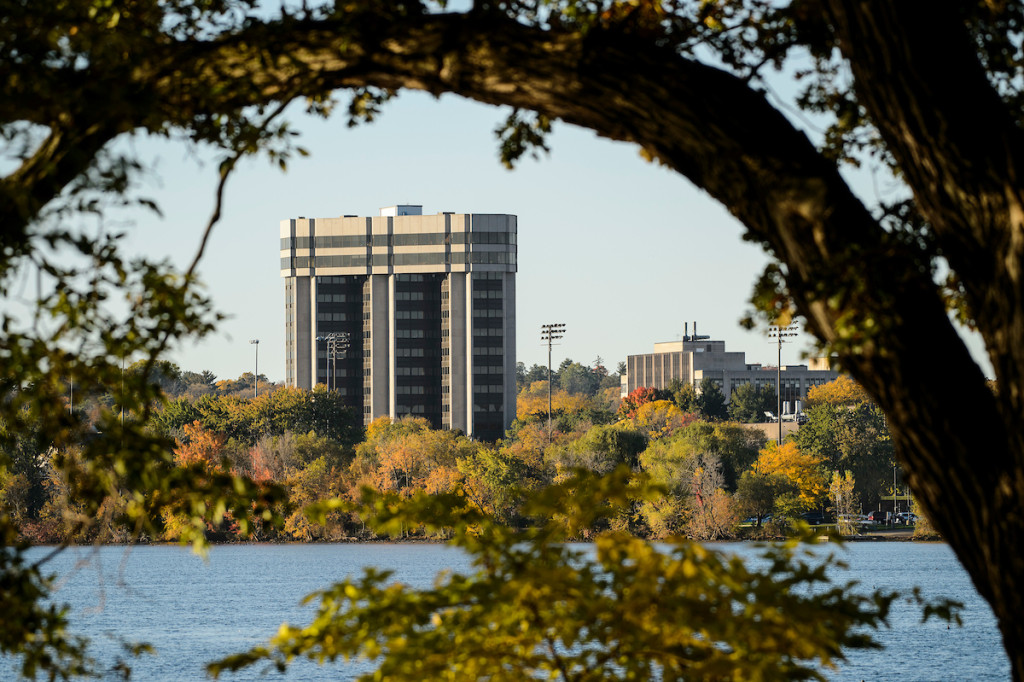 A building is shown with a lake in the foreground and a tree arching in the near foreground.