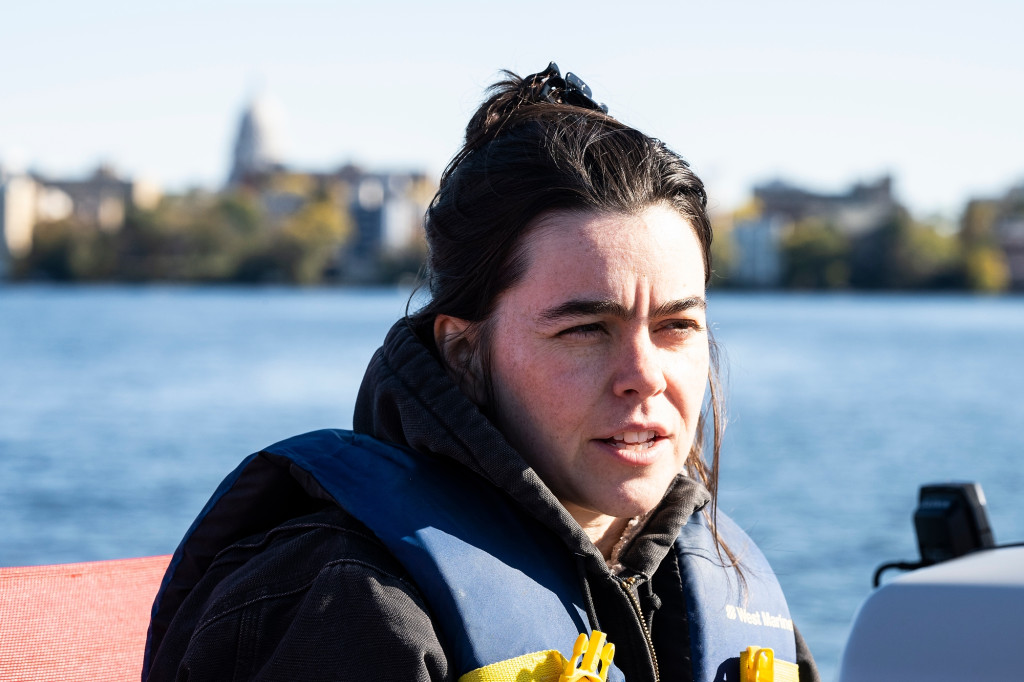 A woman wearing a warm sweatshirt is shown outside in the sun, with a city skyline behind her.