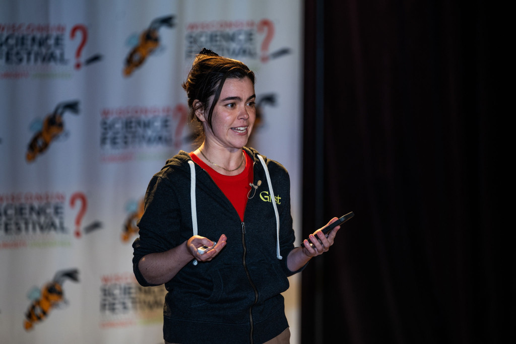 A woman is shown talking and gesticulating on stage.