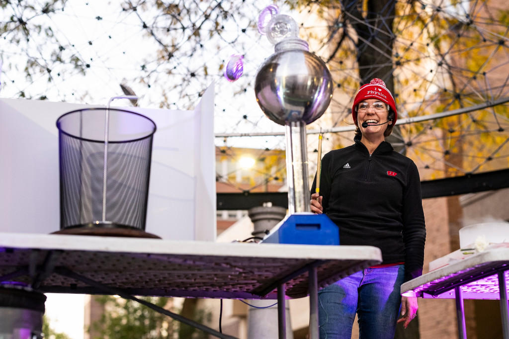 A woman stands on a stage, talking into a microphone and working with a device that collects static energy.