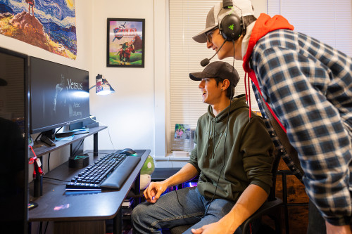 Two young men look at a computer screen; one is wearing headphones.