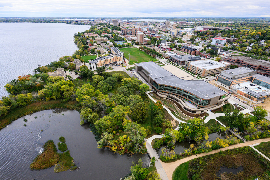 A building with curved glass walls is shown from the air. Other buildings are in the background.