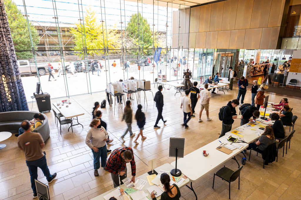 An overview of a hall with several voting booths set up and students milling about.