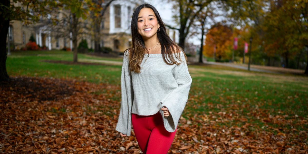 A woman is pictured standing on a grassy hill, with an academic building in the background.