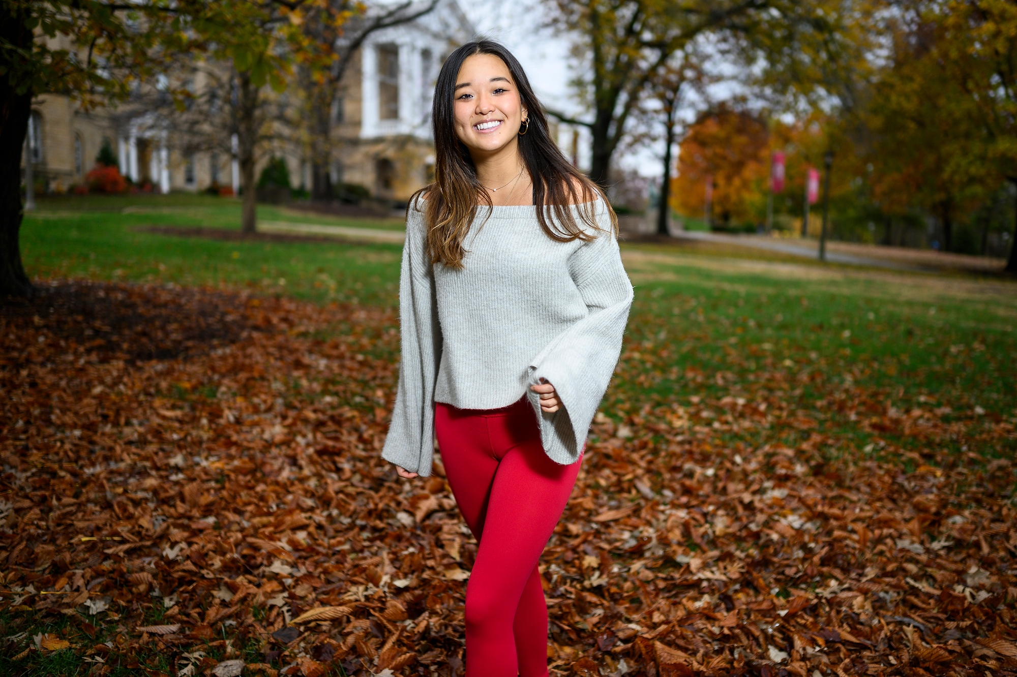 A woman is pictured standing on a grassy hill, with an academic building in the background.