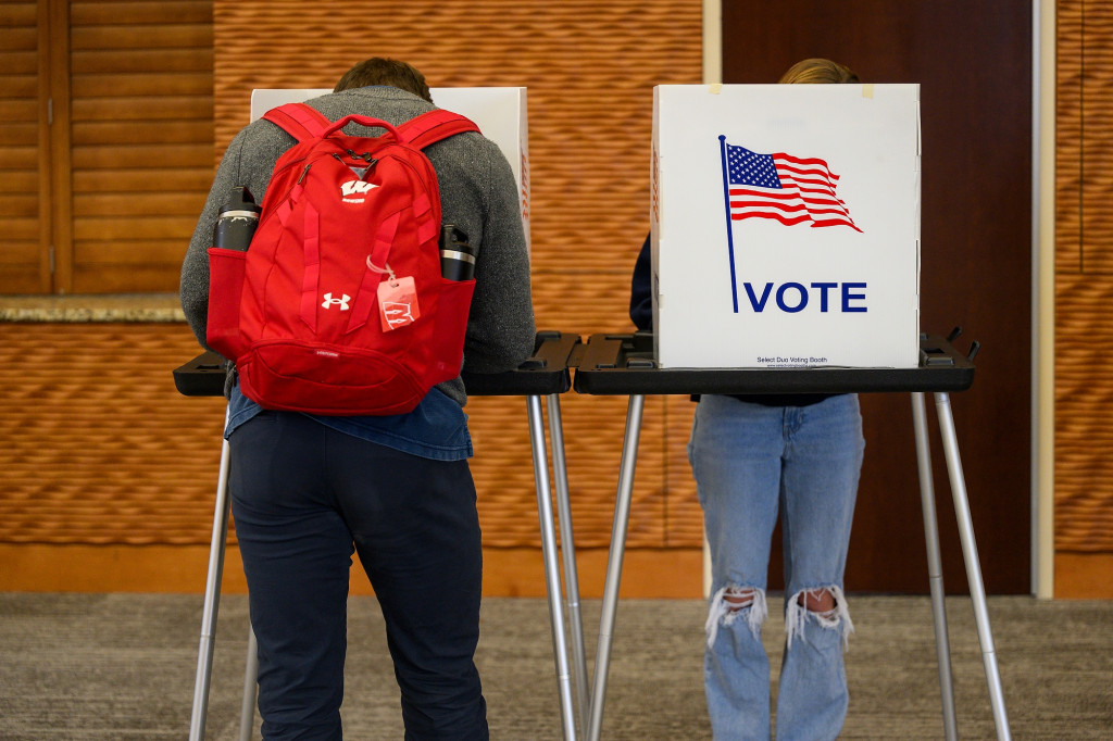 Voters stand at a voting booth, filling out a ballot.