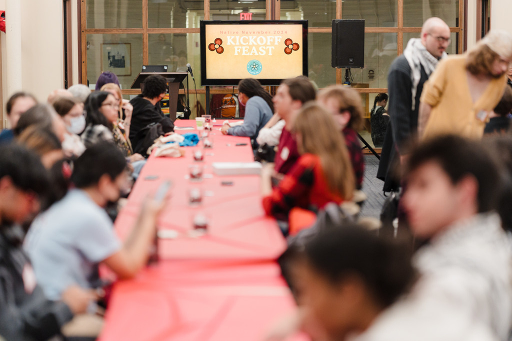 People sit on either side of a long table adorned with red table cloths.