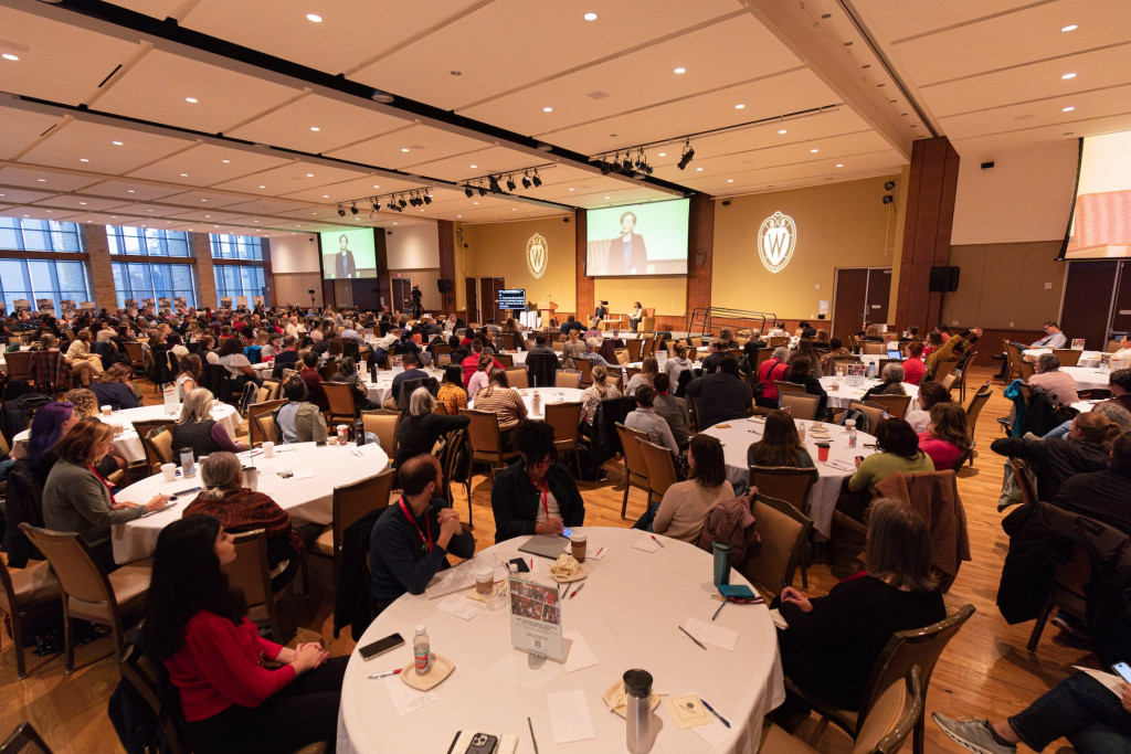 A room is full of people sitting at tables listening to a speech.