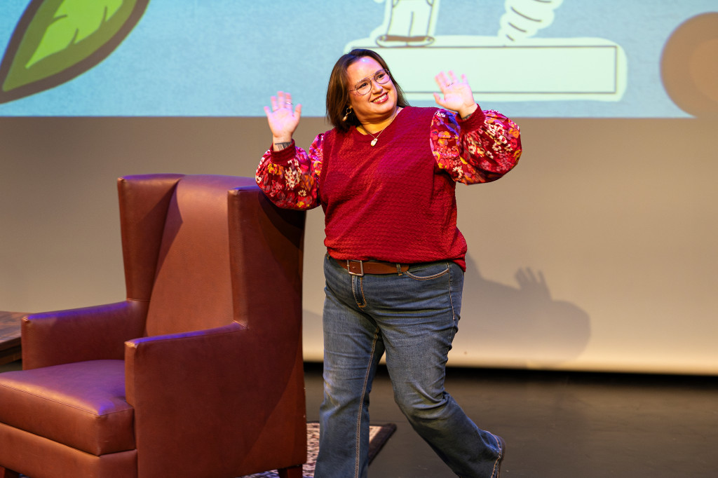 A woman waves to the audience while walking on stage.